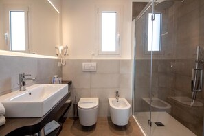 A modern bathroom with a large sink, two bidets, a glass-enclosed shower, and two windows providing natural light. - Cesare Augustus (Jesolo)