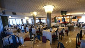 A spacious dining area with multiple tables and chairs, large windows, and a high ceiling with decorative elements. - Cesare Augustus (Jesolo)