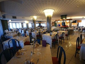 A spacious dining area with multiple tables and chairs, large windows, and a high ceiling with decorative elements. - Cesare Augustus (Jesolo)
