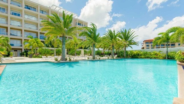Una piscina con agua cristalina azul, rodeada de palmeras y un edificio de hotel de varios pisos al fondo.