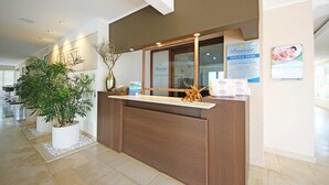 Una mesa de recepción con mostrador de madera, una planta grande en maceta y un letrero que indica el mostrador del Servicio Prestige.