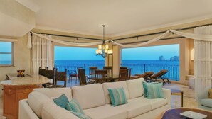 A spacious living area with a large sofa, dining table, and chairs, overlooking a scenic ocean view.
