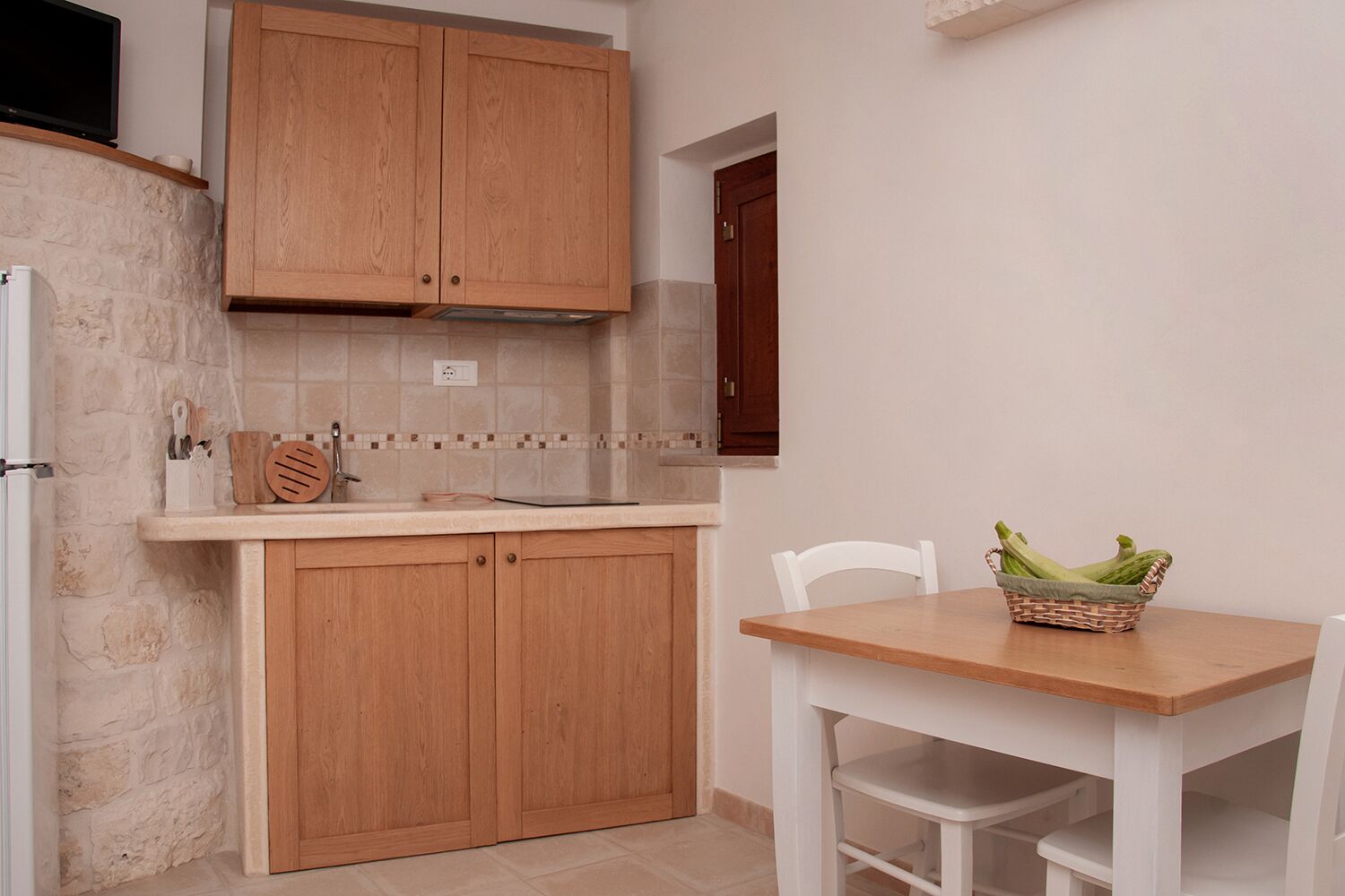 A kitchen with wooden cabinets, a countertop, and a table with a basket of vegetables.