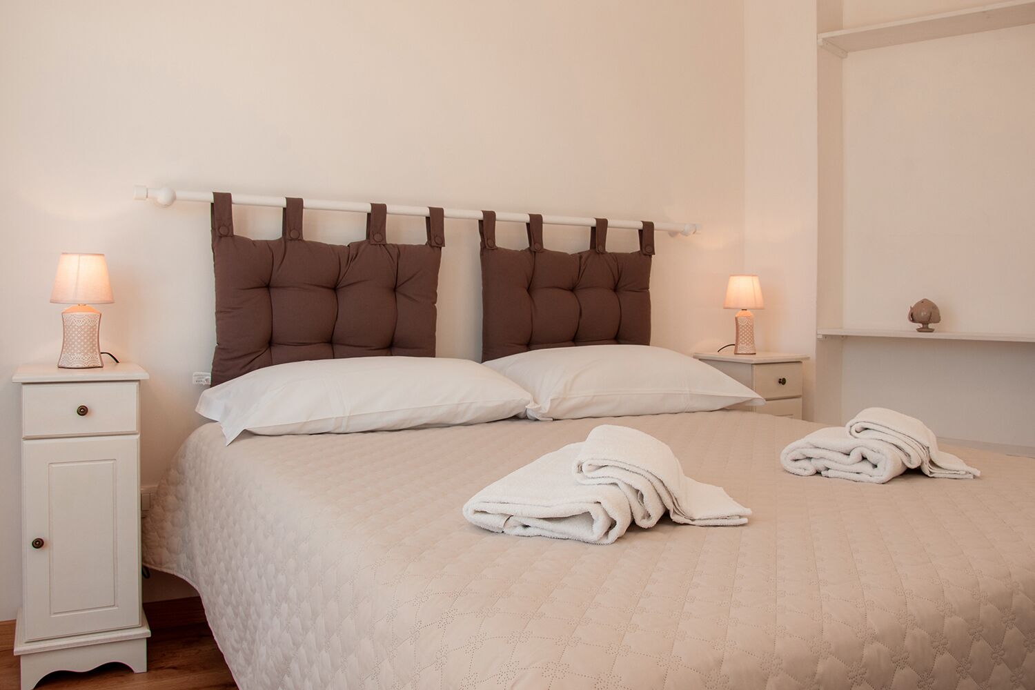 Un lit bien fait, avec deux oreillers, une tête de lit ornée de panneaux marron et deux tables de chevet avec des lampes.