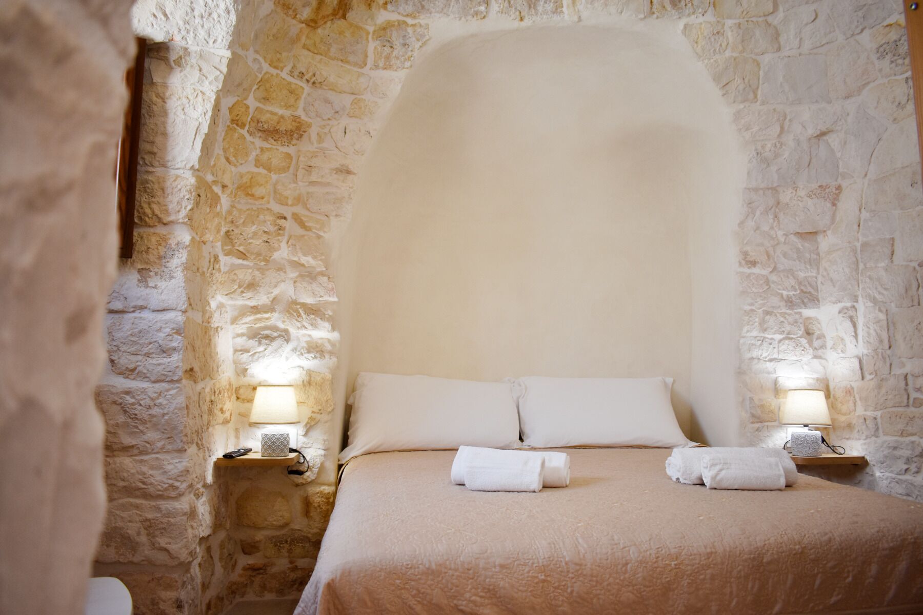A room with a stone wall, a bed with white linens, and two bedside lamps.