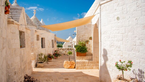 Un camí de pedra estret flanquejat per edificis blancs amb arquitectura tradicional, incloent teulades còniques i petites finestres.