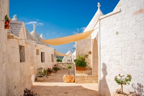 A narrow stone pathway flanked by white buildings with traditional architecture, including conical roofs and small windows.