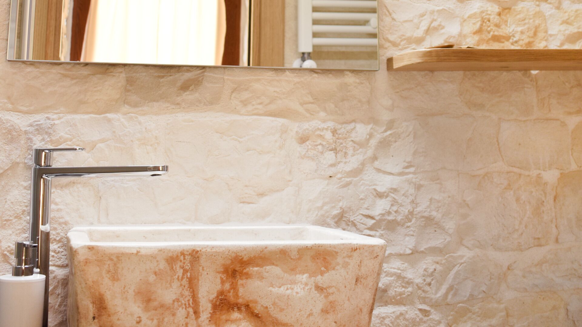 Un baño con lavamanos de mármol, grifo cromado y pared de piedra.