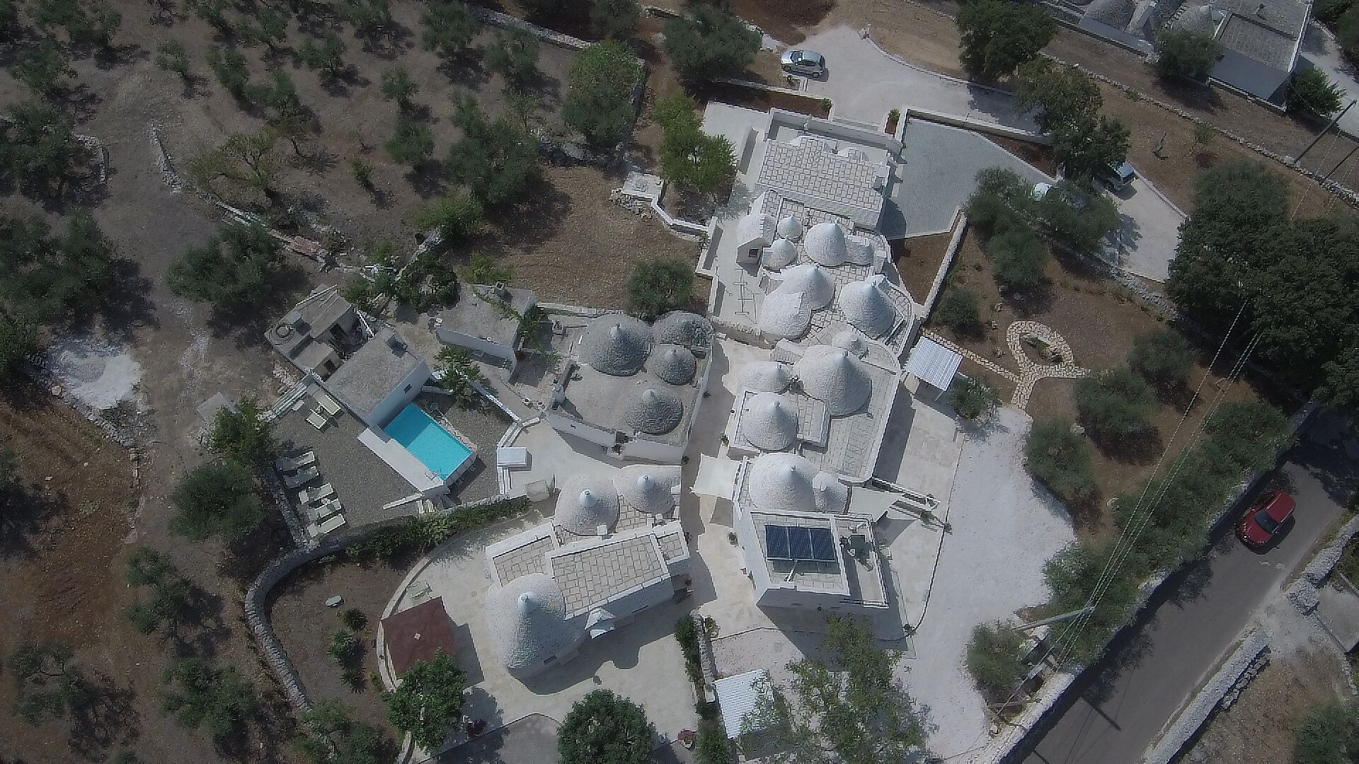An aerial view of a property with multiple buildings, a swimming pool, and surrounding greenery.