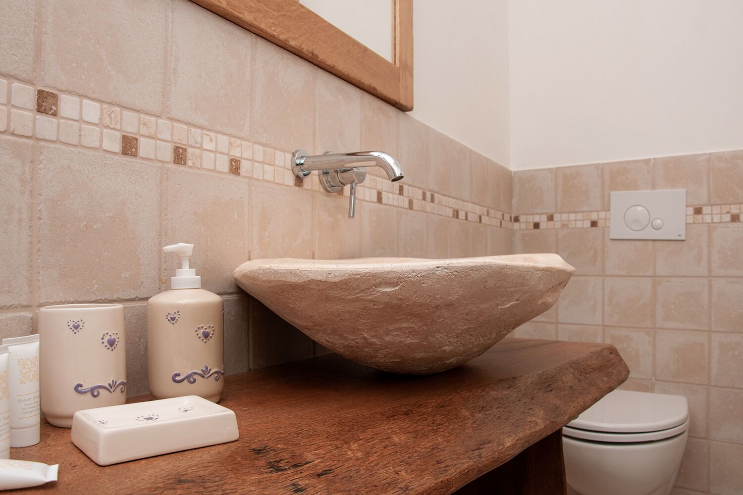 Un baño con lavamanos de piedra, encimera de madera y un espejo sobre el lavamanos.