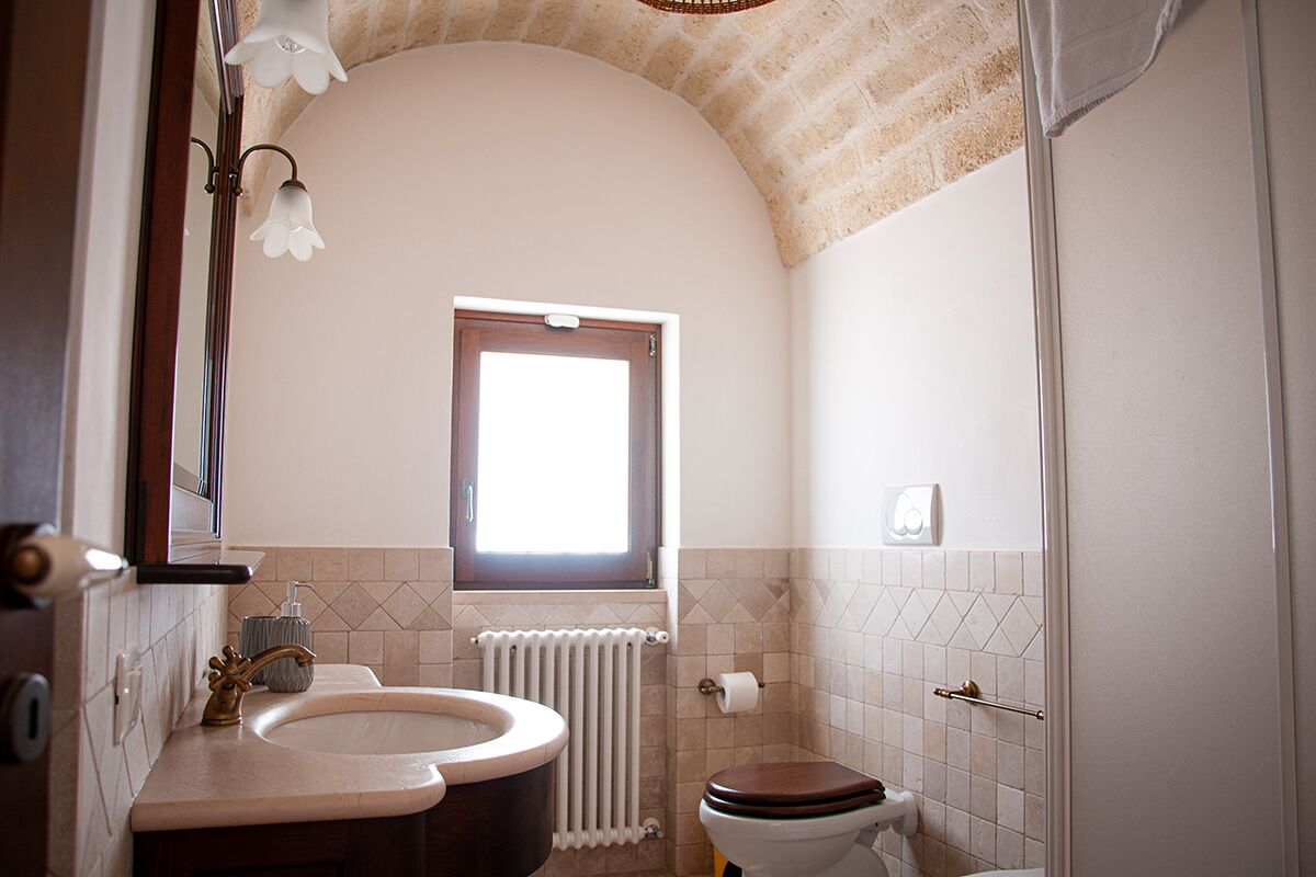 A bathroom with a double sink, a toilet, a window, and a radiator.
