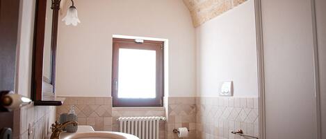 A bathroom with a double sink, a toilet, a window, and a radiator.