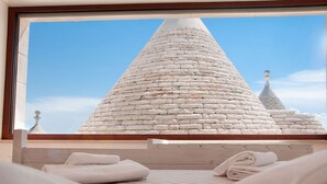 Habitació d'hotel amb una finestra gran que dona a una construcció de pedra.