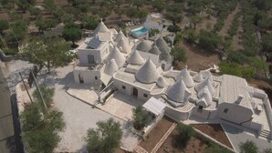 Vista aèria d'un conjunt arquitectònic tradicional amb diverses construccions de teulades còniques, una piscina i vegetació circumdant.