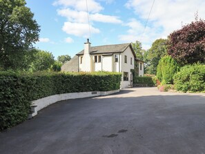 A two-story house with a white exterior, a chimney, and a driveway leading to the front door. - Greenbank Cottage (Kendal)