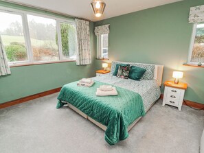 A bedroom with a bed, two bedside tables, a window, and a lamp. - Greenbank Cottage (Kendal)