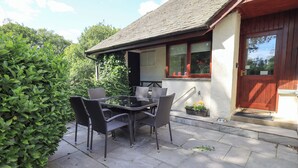 A patio with a table and chairs, a wooden door, and a window with a view of the sky. - Greenbank Cottage (Kendal)