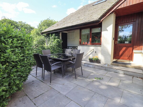 A patio with a table and chairs, a wooden door, and a window with a view of the sky. - Greenbank Cottage (Kendal)