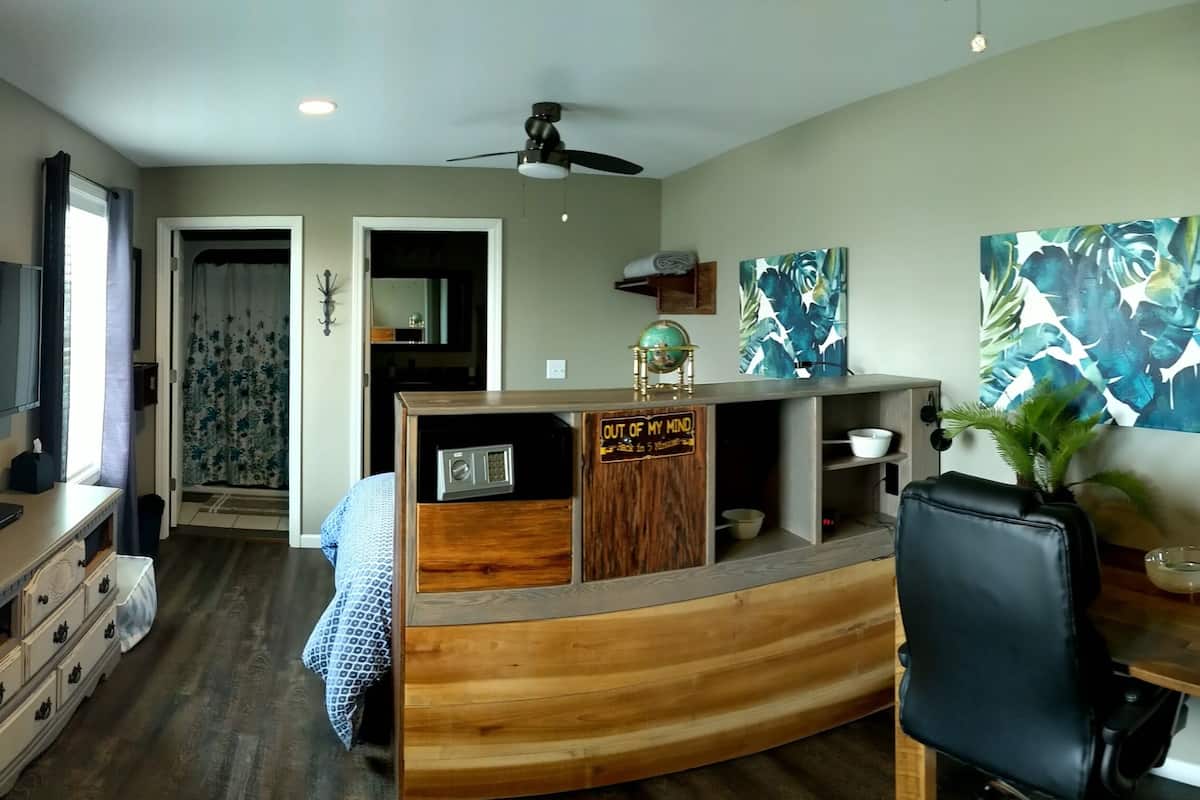 A modern living room with a curved wooden coffee table, a black leather sofa, a flat-screen TV mounted on the wall, and abstract paintings on the walls.