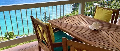 Een houten tafel en stoelen op een balkon met uitzicht op de zee.