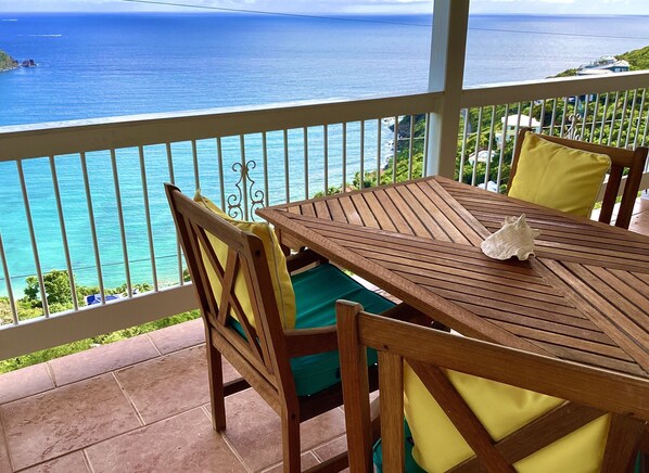 Une table et des chaises en bois sur un balcon avec vue sur l’océan.