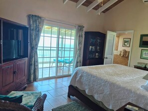 A bedroom with a large bed, a wardrobe, a television, and a view through a sliding door to an outdoor area with chairs.