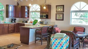 A spacious kitchen with wooden cabinets, a central island, and a dining area with wicker furniture. - Nancy's Folly Villa - Fabulous Home - overlooking dazzling Rendezvous Bay (Cruz Bay)