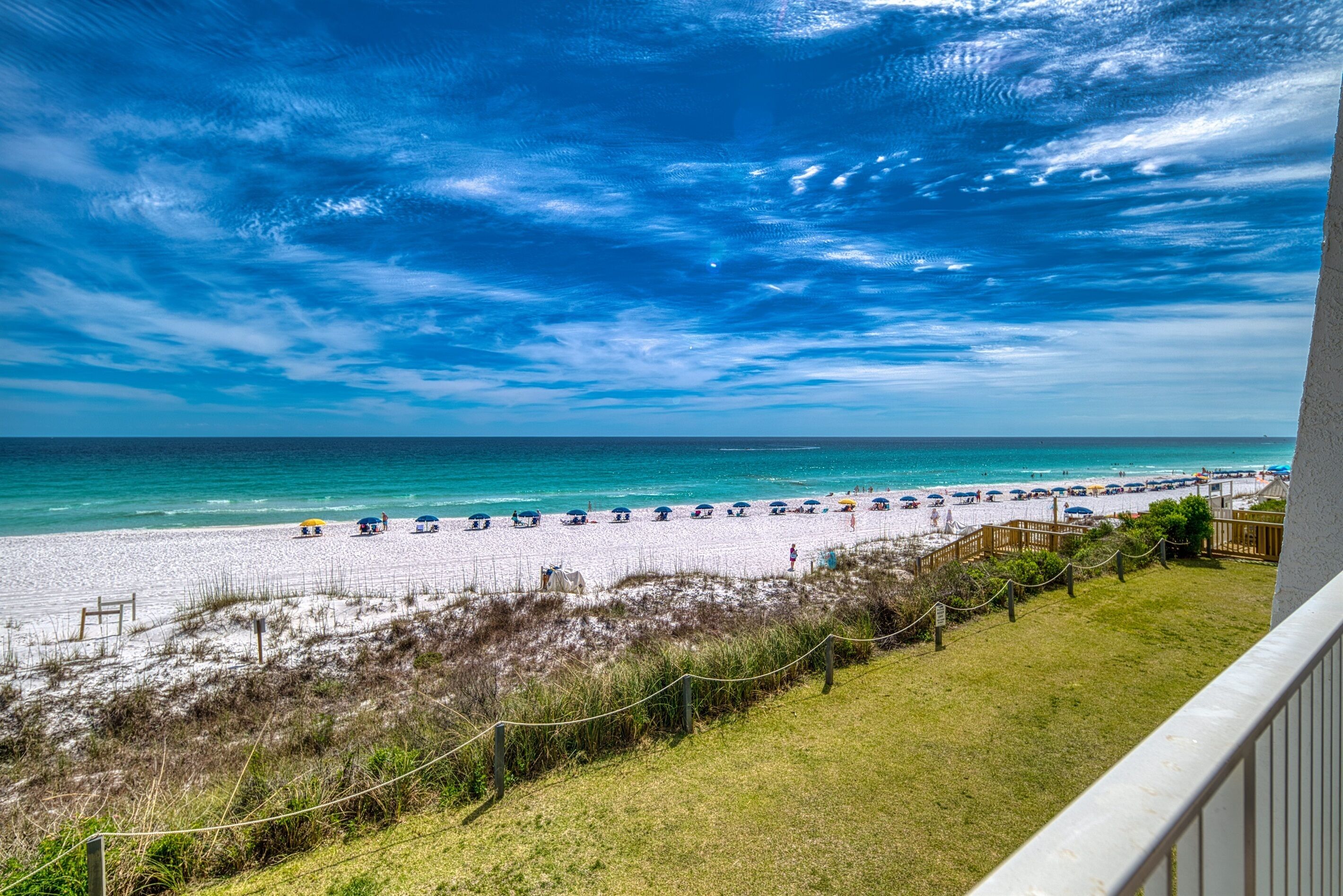 A beach with umbrellas and people, a clear sky, and a view of the ocean.