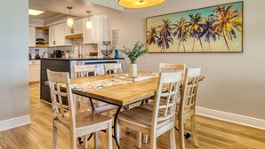 Un comedor con una mesa y sillas de madera, una lámpara colgante y un cuadro de palmeras en la pared.