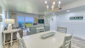 A dining area with a table, chairs, a chandelier, and a view of the outdoors. - B105 | Beachfront with Beach Service, Pool, & WiFi (Miramar Beach)