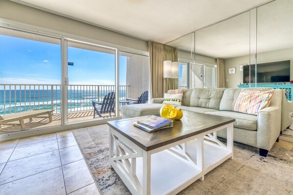 Relax in this stylish living room with a sofa, coffee table, and TV, leading to a balcony with ocean views.