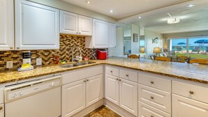 A modern kitchen with white cabinets, a granite countertop, and a built-in dishwasher. - C103 | Beachfront with Beach Service, Pool, & WiFi (Miramar Beach)