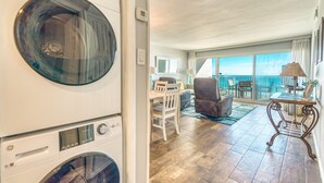 Un'area lavanderia con lavatrice e asciugatrice a carica frontale, una sala da pranzo con tavolo e sedie, e un balcone con vista sull'oceano.