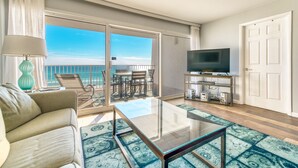 Un soggiorno moderno con un tavolino in vetro, un divano, un mobile TV e un balcone con vista sull'oceano.