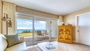 Una habitación con sof á, mesa de centro, armario de madera y puerta corrediza de vidrio que da a un patio con mobiliario exterior.
