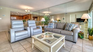 A modern living room with a sofa, two armchairs, a glass coffee table, and a kitchen in the background. - D404 | Beachfront with Beach Service, Pool, & WiFi (Miramar Beach)