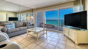 A modern hotel room with a balcony, a sofa, a TV, and a glass coffee table. - D404 | Beachfront with Beach Service, Pool, & WiFi (Miramar Beach)