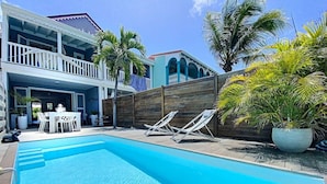 A swimming pool with lounge chairs, a dining area with a table and chairs, and a wooden fence.