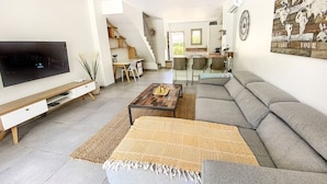 A modern living room with a flat-screen TV, a sofa, a coffee table, and a staircase leading to a kitchen.
