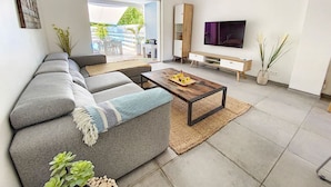 A modern living room with a grey sectional sofa, a wooden coffee table, and a flat-screen TV mounted on the wall.