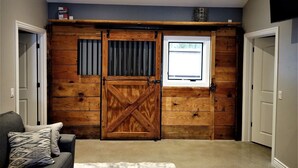 A room with a large wooden barn-style door, a window, and a gray couch with patterned cushions.