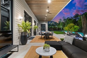 A modern outdoor patio with a dining table, black sofa, and potted plants.