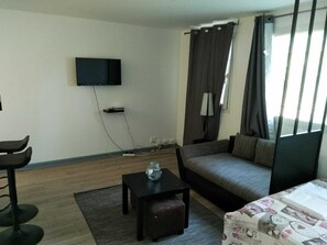 Un salon moderne avec un canapé, une table basse, un téléviseur fixé au mur et une fenêtre avec des rideaux.