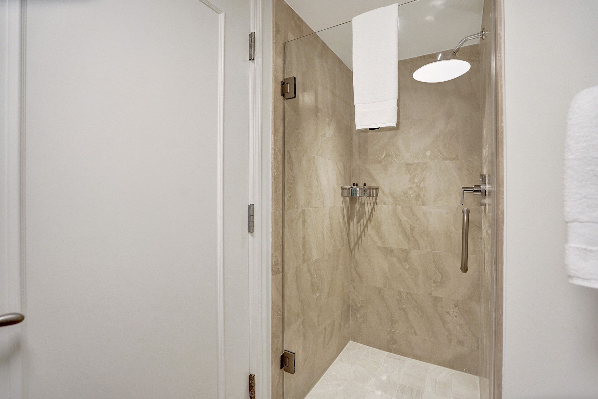 A modern bathroom with a glass shower enclosure, a handheld showerhead, and a wall-mounted faucet.