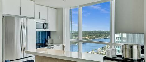 A modern kitchen with a large window, a stainless steel refrigerator, a microwave, and a toaster.