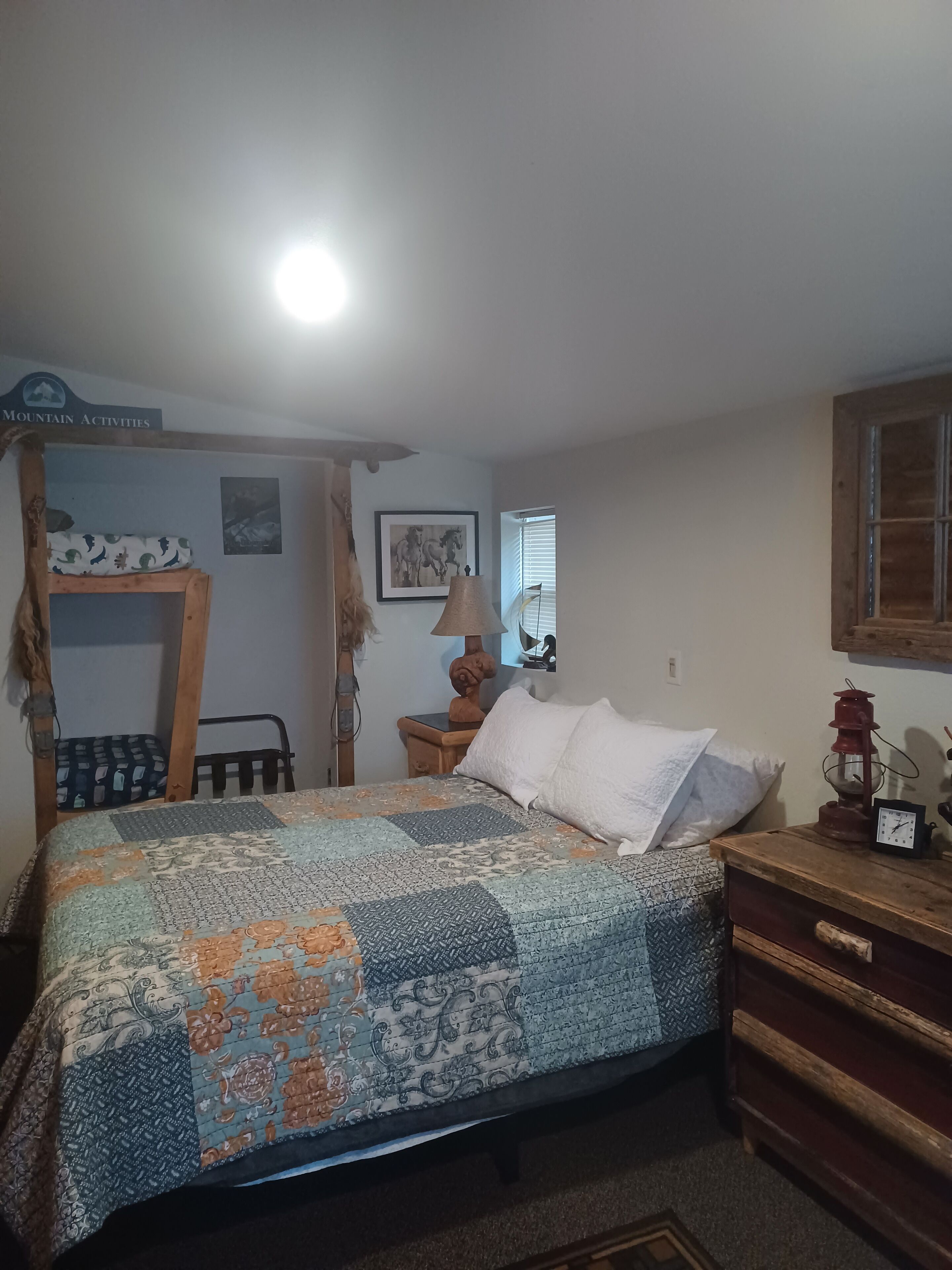 A bedroom with a bed, a wooden dresser, a nightstand, a lamp, and a sign above the bed.