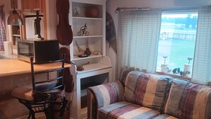 Un salón acogedor con un sofá a rayas, techo de madera, una mesita con un mensaje y vistas a un lago a través de una ventana.