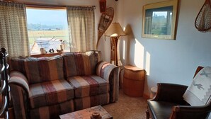 Una sala de estar acogedora con un sofá de cuadros, una mesa de centro de madera, un sillón de cuero, una lámpara y un cuadro en la pared.