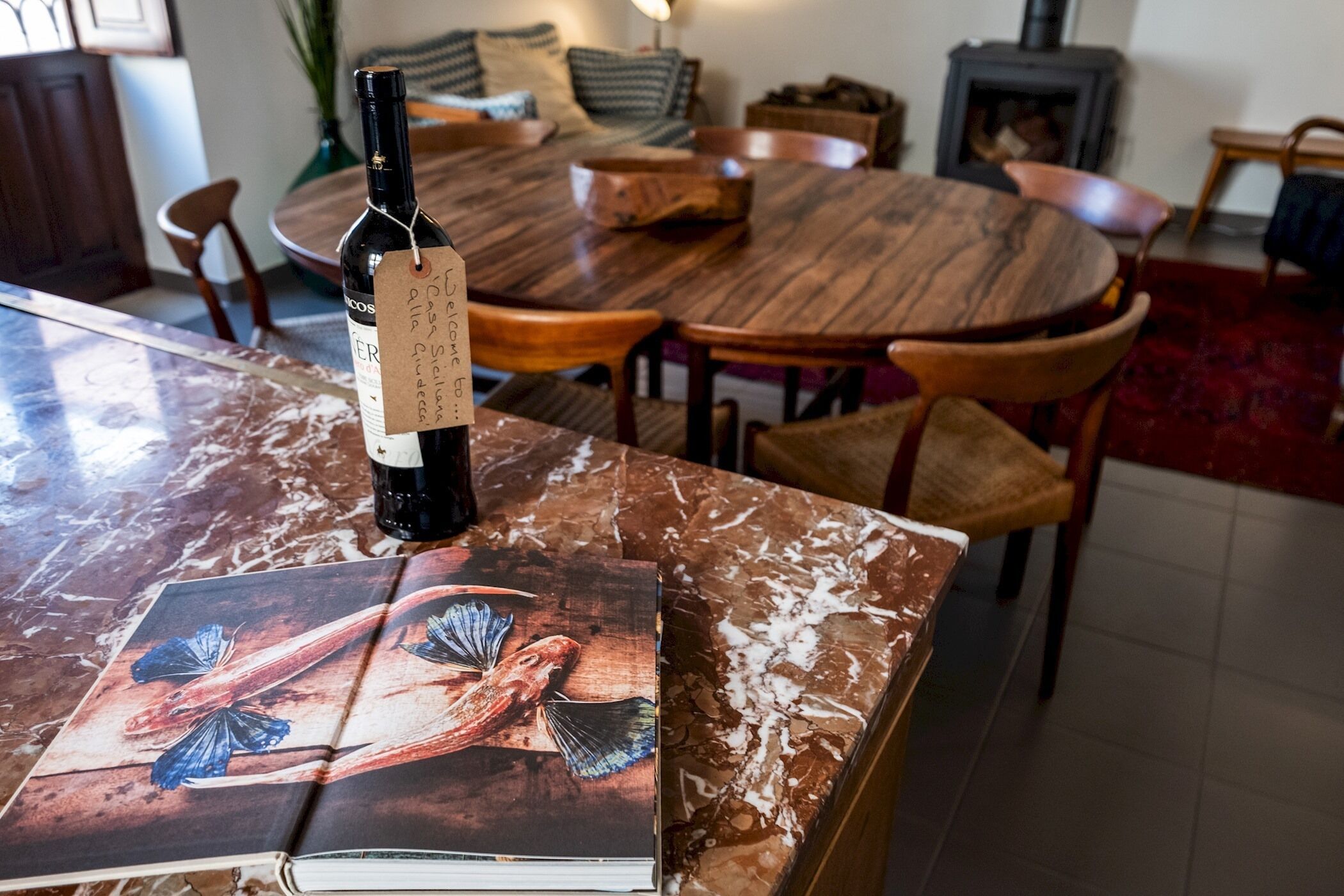 Uma garrafa de vinho sobre uma mesa de mármore com um livro que apresenta uma ilustração de peixe.