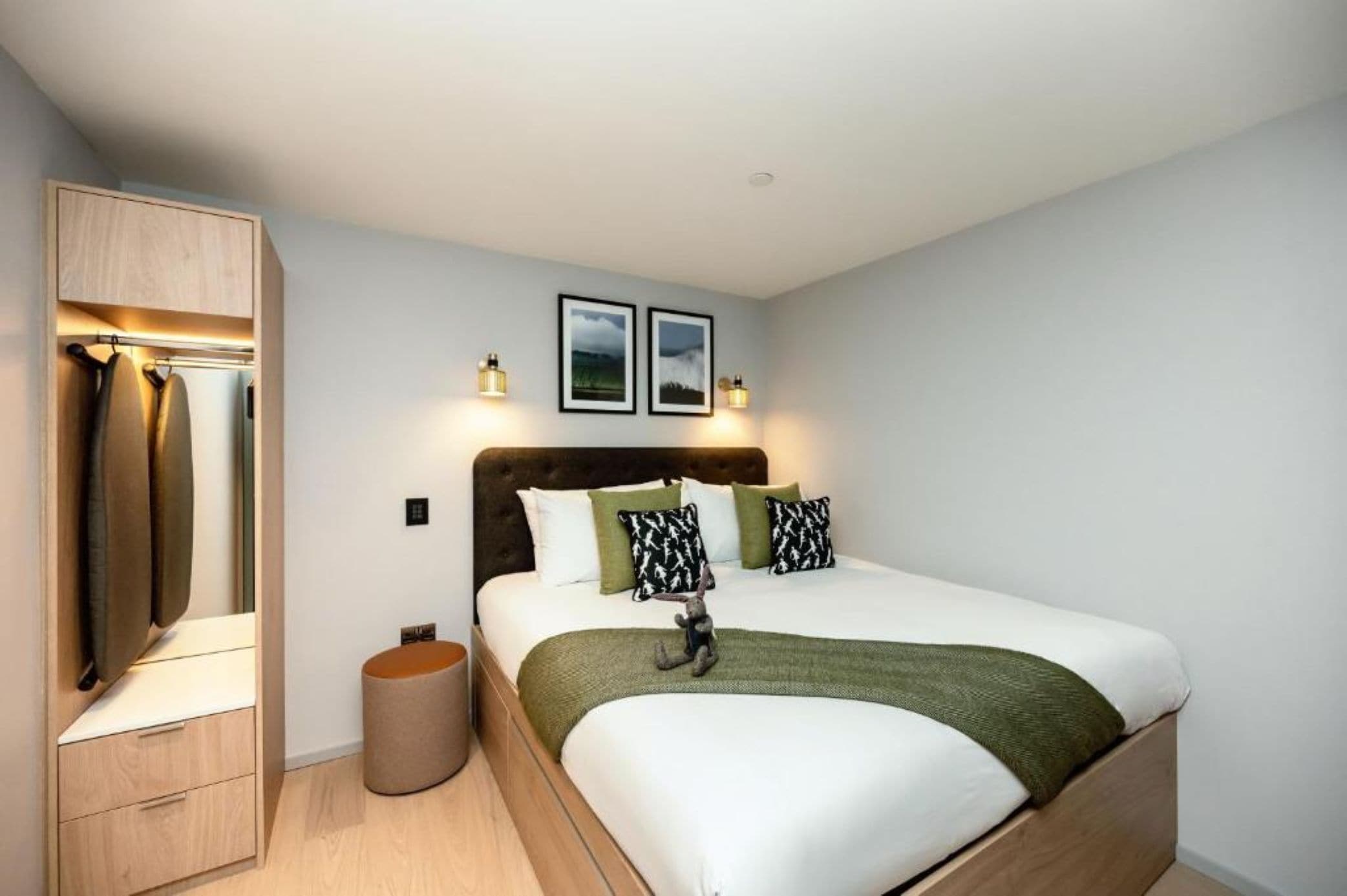 A bedroom with a bed, a wardrobe, a bedside table, and two wall-mounted lights.